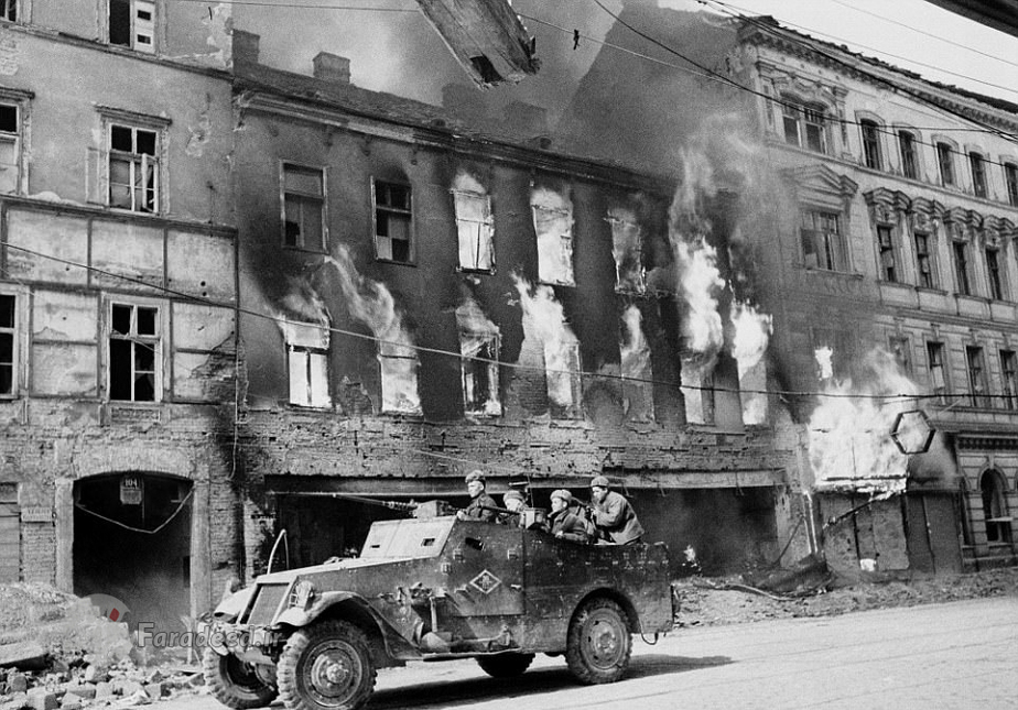 یک خودروی زرهی در وین – پشت این خودرو، ساختمانی در حال آتش گرفتن است